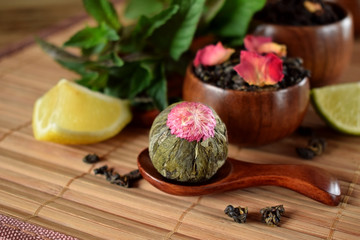 Blossom tea ball and leaf tea with rose petals in wooden cups and spoon