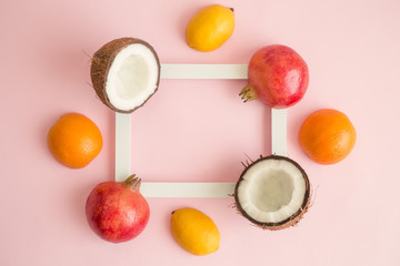 Exotic fruits around photo frame on rose background abstract.