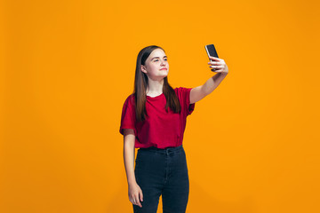 The happy teen girl standing and smiling against orange background.