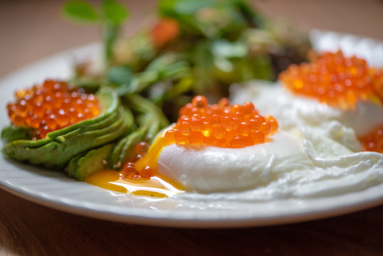 Delicious breakfast with poached eggs, red caviar and sliced avocado