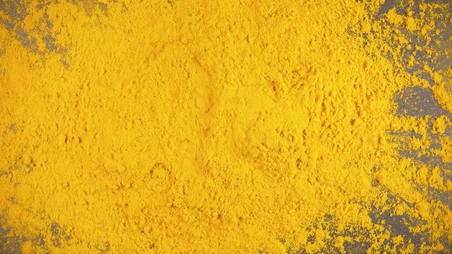 Slow motion turmeric powder dry spice drops on a gray background from under the camera