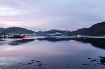 A view of Holy Loch, from Sandbank, near Dunoon in Argyll Scotland as the sun sets out of shot casting a beautiful blue, calm hue across the sky reflected in the waters of the loch.