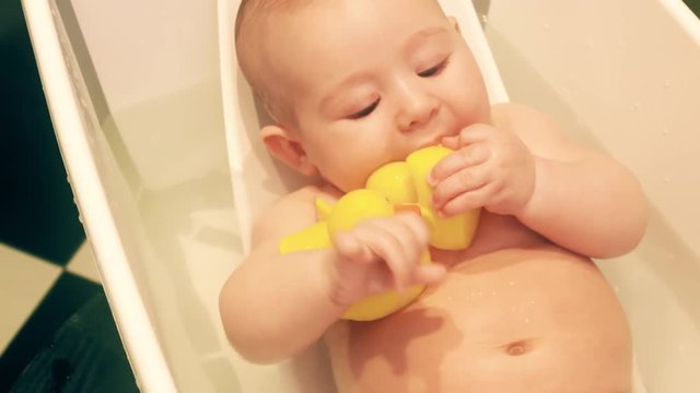 Funny baby girl holds rubber ducks in a bath tub