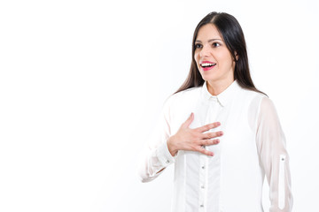 Young beautiful brunette woman surprised with white shirt right hand on heart and looking away, isolated on white background