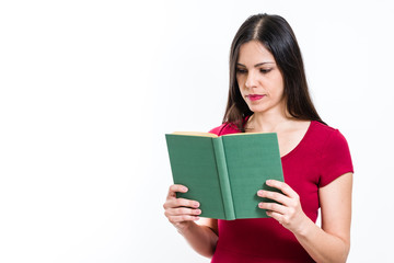 Fototapeta premium Young beautiful brunette woman serious with red shirt, reading a green cover book, looking to the book, isolated on white background