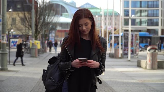 Young Swedish girl walking in the city in the spring, typing on her phone