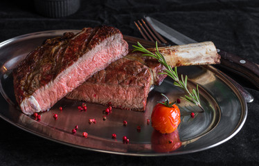 Single tomahawk rib steak on silver dish next to roasted cherry tomatoes