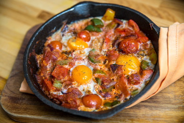 Shakshuka - eggs in tomato sauce in a skillet over wooden background.