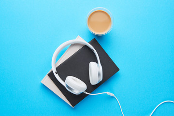 Top view of white headphones, notebooks and coffee on blue background with copy space. Flat lay.
