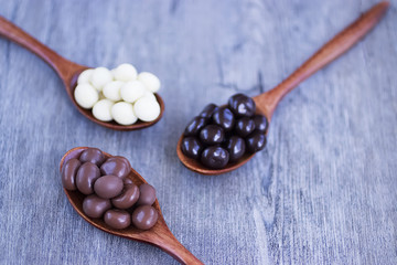 Grains of coffee in glaze of white, milky, and dark chocolate in wooden spoons.