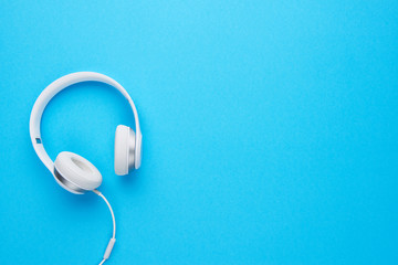 Top view of white headphones on blue background with copy space. Flat lay.