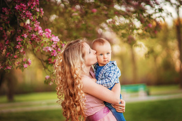 Mother, beautiful girl blonde woman, with a baby in her arms for a walk in a flower garden.