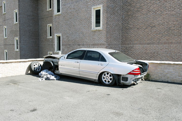 A wrecked silver color car in a parking lot in front of an office building