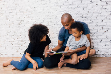 African American father reading a fairy tale fable story for kids at home. Happy family sitting on...