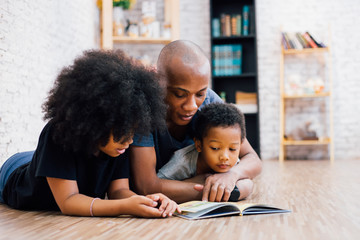 African American father reading a fairy tale fable story for kids at home. Happy family lying on...