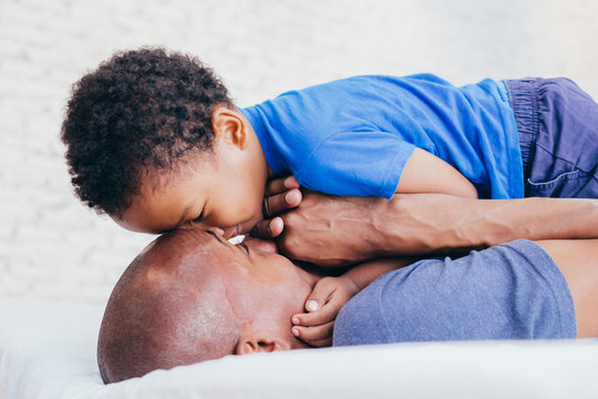 African American family of two, son looking at father on bed at home