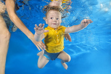 Fototapeta na wymiar Mom teaches a little boy in a yellow shirt to swim underwater in the pool
