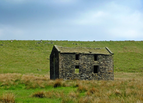 an old abandoned stone farmhouse in green pasture on high pennine moorland with bright blue sky