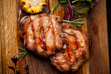 two grilled steaks with corn and salad on a wooden plank