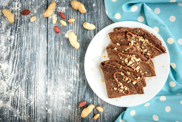 Chocolate oat pancakes with caramel and nuts with cup of coffee on blue fabric and grey wooden table.