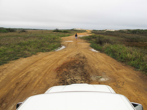 Um homem caminhando em estrada a frente de um veiculo