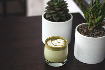Cup of hot matcha green tea latte with plant on table. Top view of green tea milk. Cappuccino latte art in glass. Flat lay style.