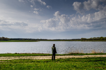 The guy is standing in front of the lake. The guy is traveling and looking at the lake