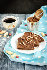 Chocolate oat pancakes with caramel and nuts with cup of coffee on blue fabric and grey wooden table.