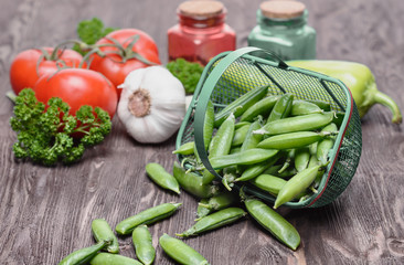 Pods of green peas, a branch of red tomatoes and other vegetables are on a wooden table