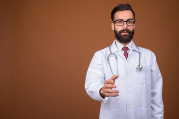 Young handsome bearded Persian man doctor against brown backgrou