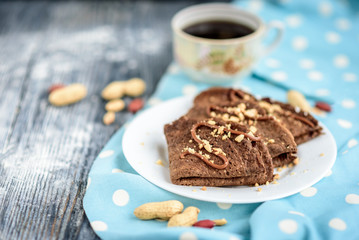 Chocolate oat pancakes with caramel and nuts with cup of coffee on blue fabric and grey wooden table.