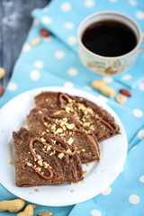 Chocolate oat pancakes with caramel and nuts with cup of coffee on blue fabric and grey wooden table.