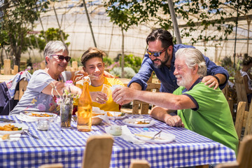 three different mixed generations at the table outdoor in a natural restaurant having fun together. drink and eat fresh food and have a nice leisure. people mixed ages grandfathers, father and son