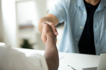 Close up of multiracial handshake at office desk. Caucasian worker shaking hand of black colleague, welcoming at new workplace, greeting, being promoted. Cooperation, support, making agreement concept