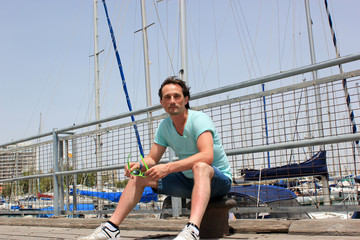 Young man sitting on bollard on pier with barrier in marina