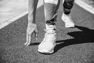 Woman tying jogging shoes black & white tonned. Great running outdoors on a sunny day.