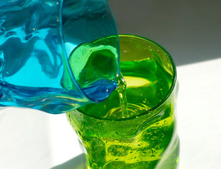 Two glasses of colored glass. Refreshing drink pours from one glass to another glass.