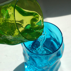 Two glasses of colored glass. Refreshing drink pours from one glass to another glass.
