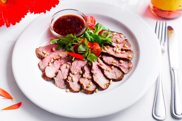 Duck breast roasted with tomato, baby spinach with berry sauce on a white plate