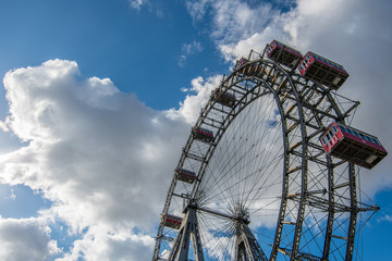 A huge Victorian Metal Ferris Wheel in a large public park in Vienna, Austria with a blue sky and white fluffy clouds above.