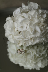 A bouquet of white hydrangeas and engagement rings lie on a glass table. Close-up vertical photo