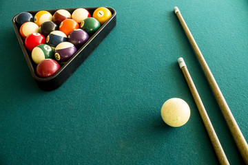 Billiard balls arranged in a triangle on a green table with two cue sticks