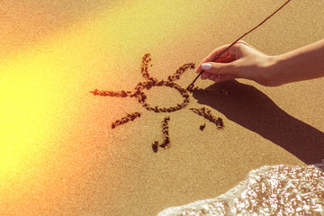 A woman's hand draws the sun on the sand by the sea, the glow effect