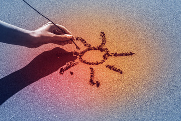 A woman's hand draws the sun on the sand by the sea, the glow effect