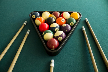 Symmetric view of billiard balls arranged in a triangle with cue sticks on green table