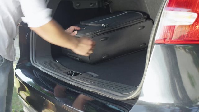 CLOSE UP: Unrecognizable young traveler packing baggage in the spacious boot of his large black car parked in the sunny suburban driveway. Unknown man in white shirt putting travel bags in his SUV.