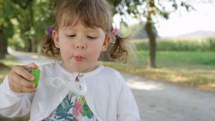 PORTRAIT: Playful young daughter tries to blow a soap bubble in tree avenue.