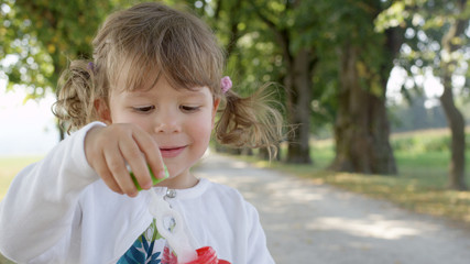 PORTRAIT: Playful baby daughter blowing soap bubbles during family trip to park.