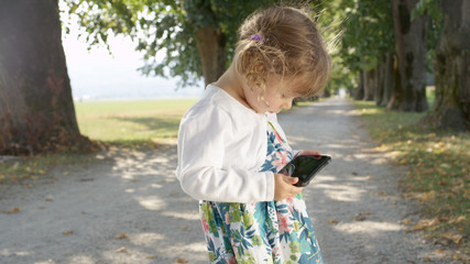 CLOSE UP: Toddler girl types on mother's high tech smart phone while at the park
