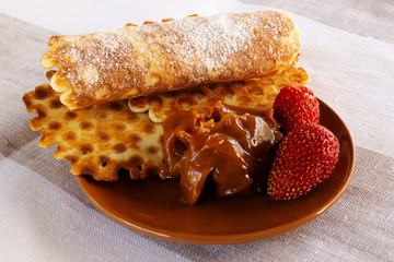 A homemade dessert made from baked goods, chocolate pasta and ripe strawberry berries, laid on a round porcelain plate of brown color.